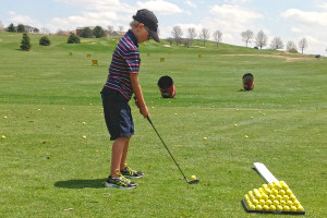 A young boy on the driving range prepared to hit a ball.