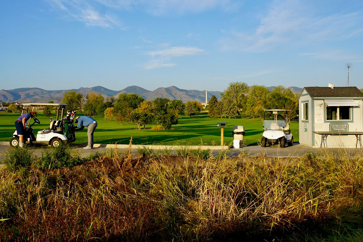 A view of golfers in a golf cart parked near the starter shack with mountains in the background