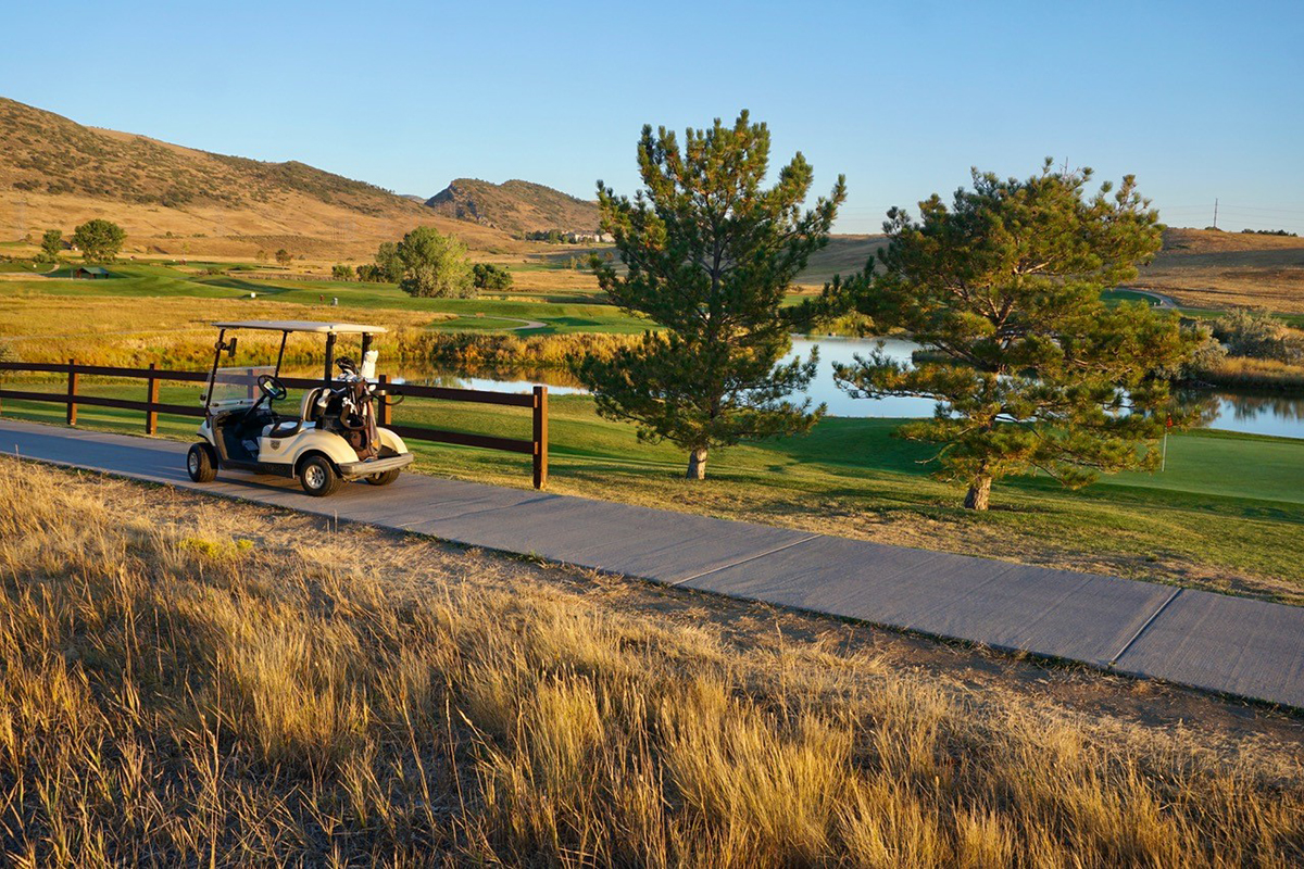 A golf cart parked on the path near a green that overlooks a pond and mountain views